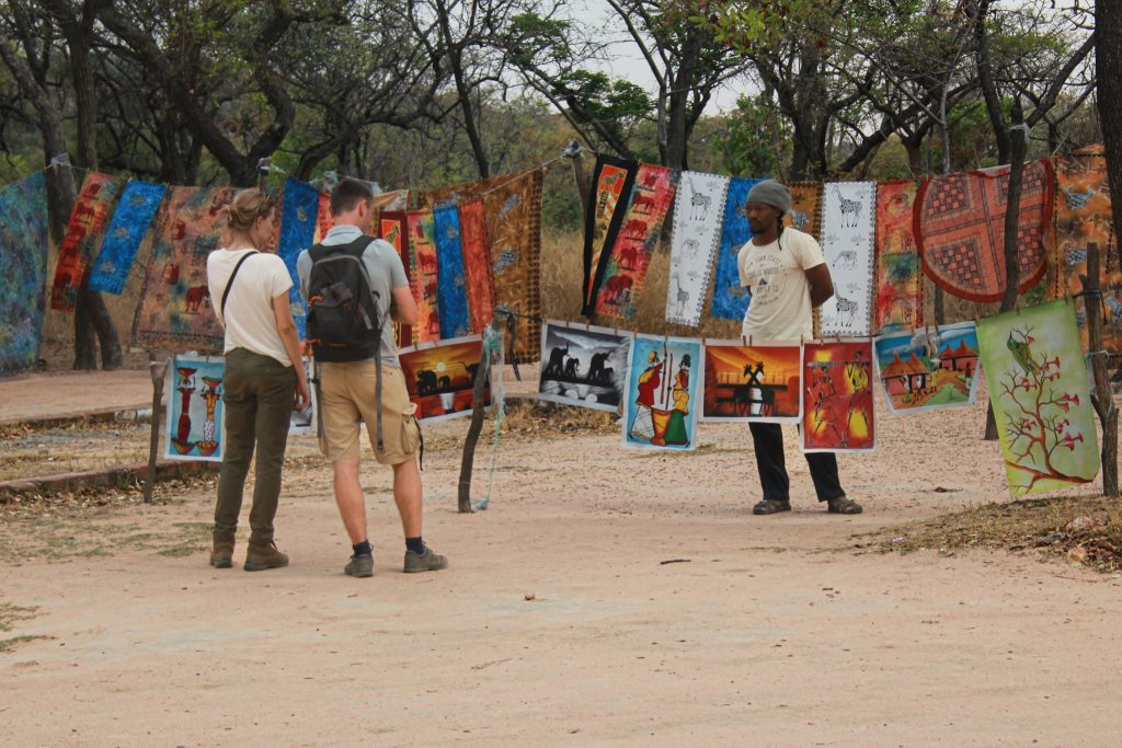 Guests browsing traditional Zimbabwean paintings and artwork at a craft market