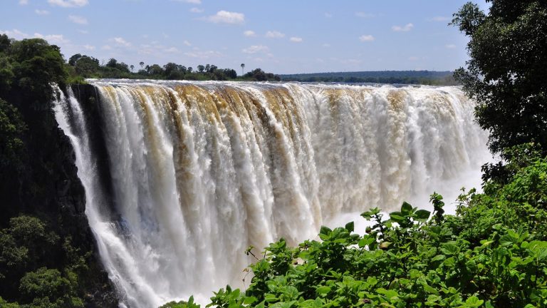 Victoria Falls peak flow wide shot Zimbabwe Zambezi River full curtain lush green